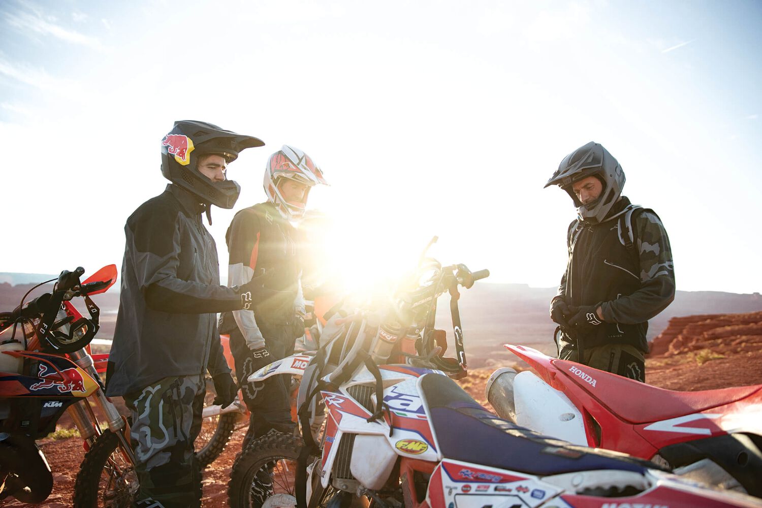 A group of enduro riders resting, a large lens flare has them in silhouette.